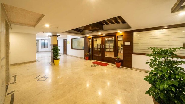A spacious lobby with a polished marble floor, wooden doors, and potted plants. - Midtown Suites  Marathahalli (Bengaluru)