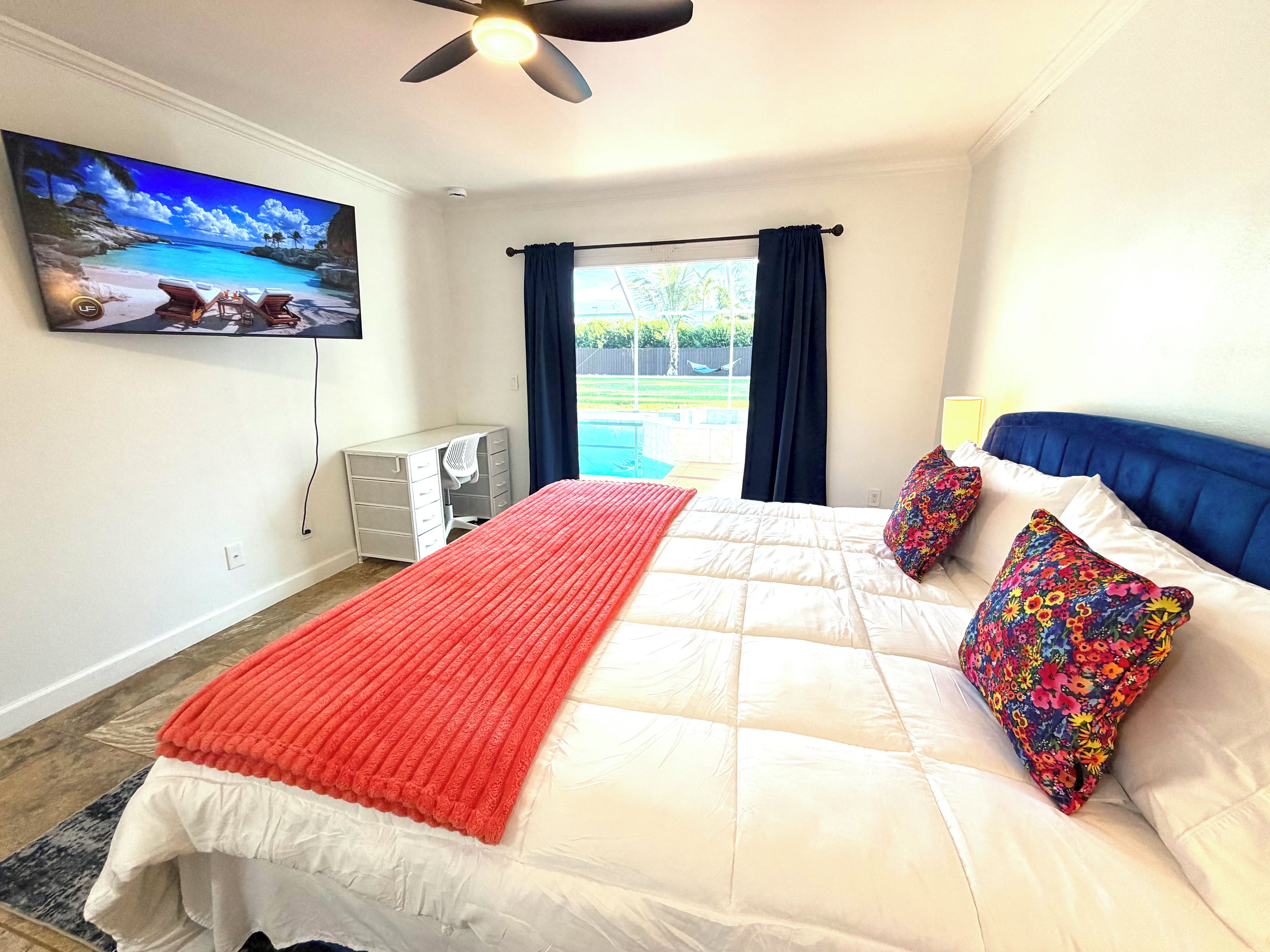 A bedroom with a bed, a desk, a TV, and a view of the outdoors.
