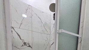 Ducha con azulejos de mármol y puerta de cristal.