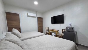 Habitación de hotel con dos camas, televisor, cafetera y una mesita.