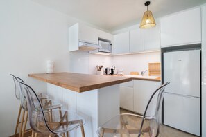 Une cuisine moderne avec des meubles blancs, un plan de travail en bois, un four à micro-ondes encastré et un réfrigérateur.