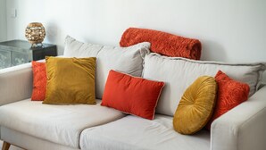 Ein weißes Sofa mit vielen Kissen in verschiedenen Farben, ein kleiner runder Tisch und ein dekorativer Gegenstand auf einem Beistelltisch.