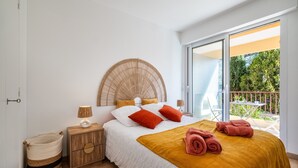 Ein Schlafzimmer mit Bett, Nachttisch, Lampe, Korb und Balkon mit Aussicht.