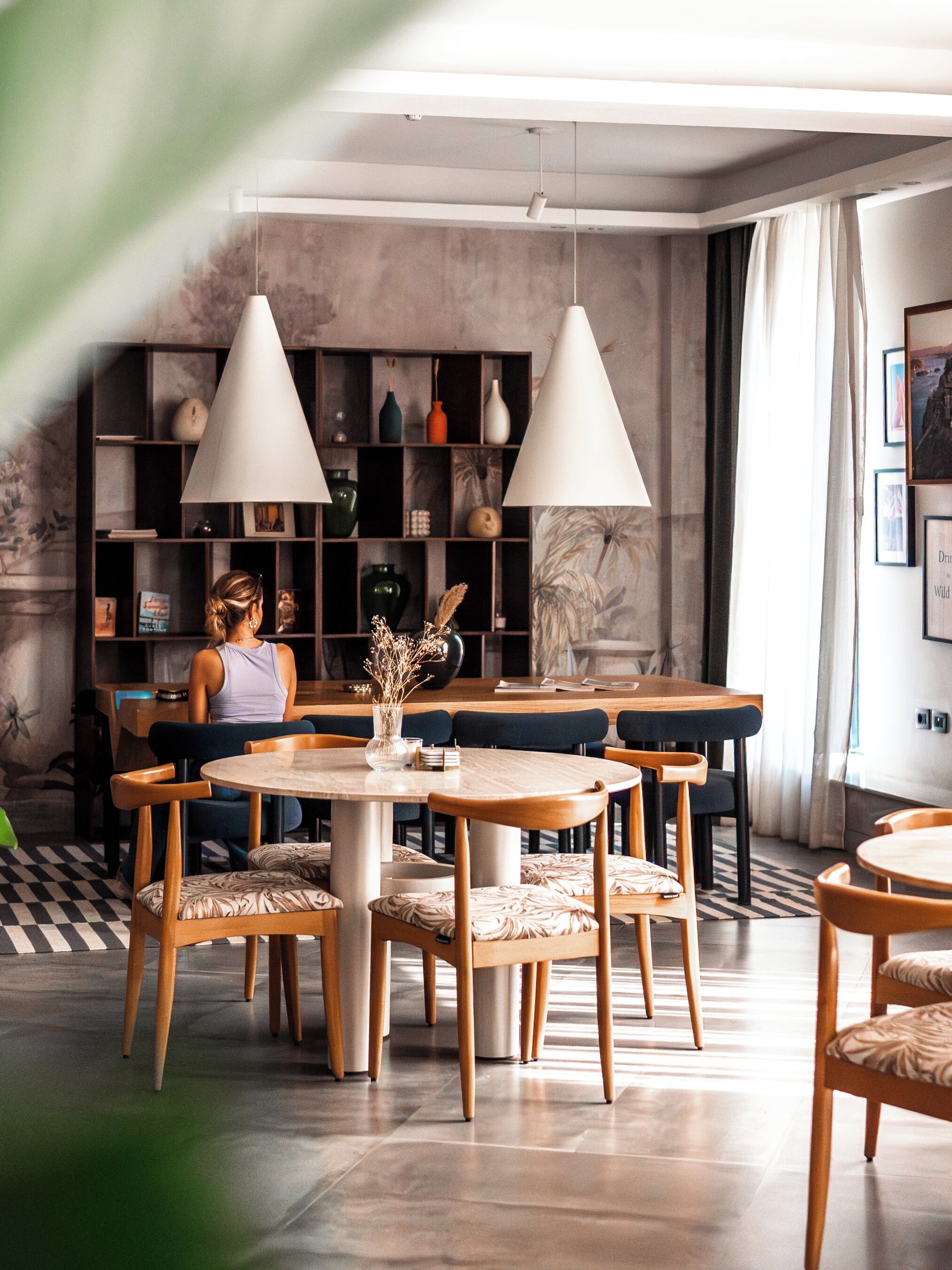 Een moderne eetruimte met houten tafels en stoelen, een ronde centrale tafel met een vaas, en hanglampen.