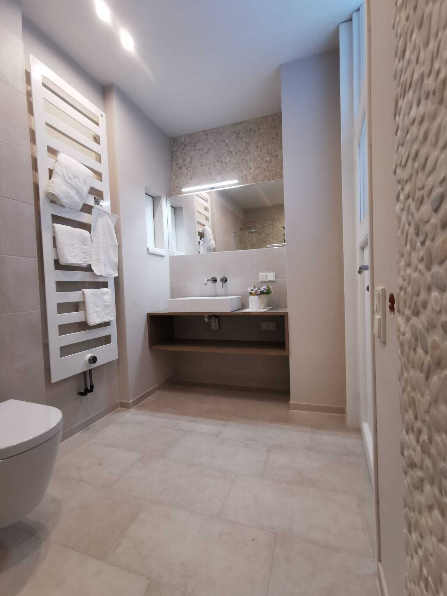 A bathroom with a toilet, a towel rack, a sink, a mirror, and a shower.