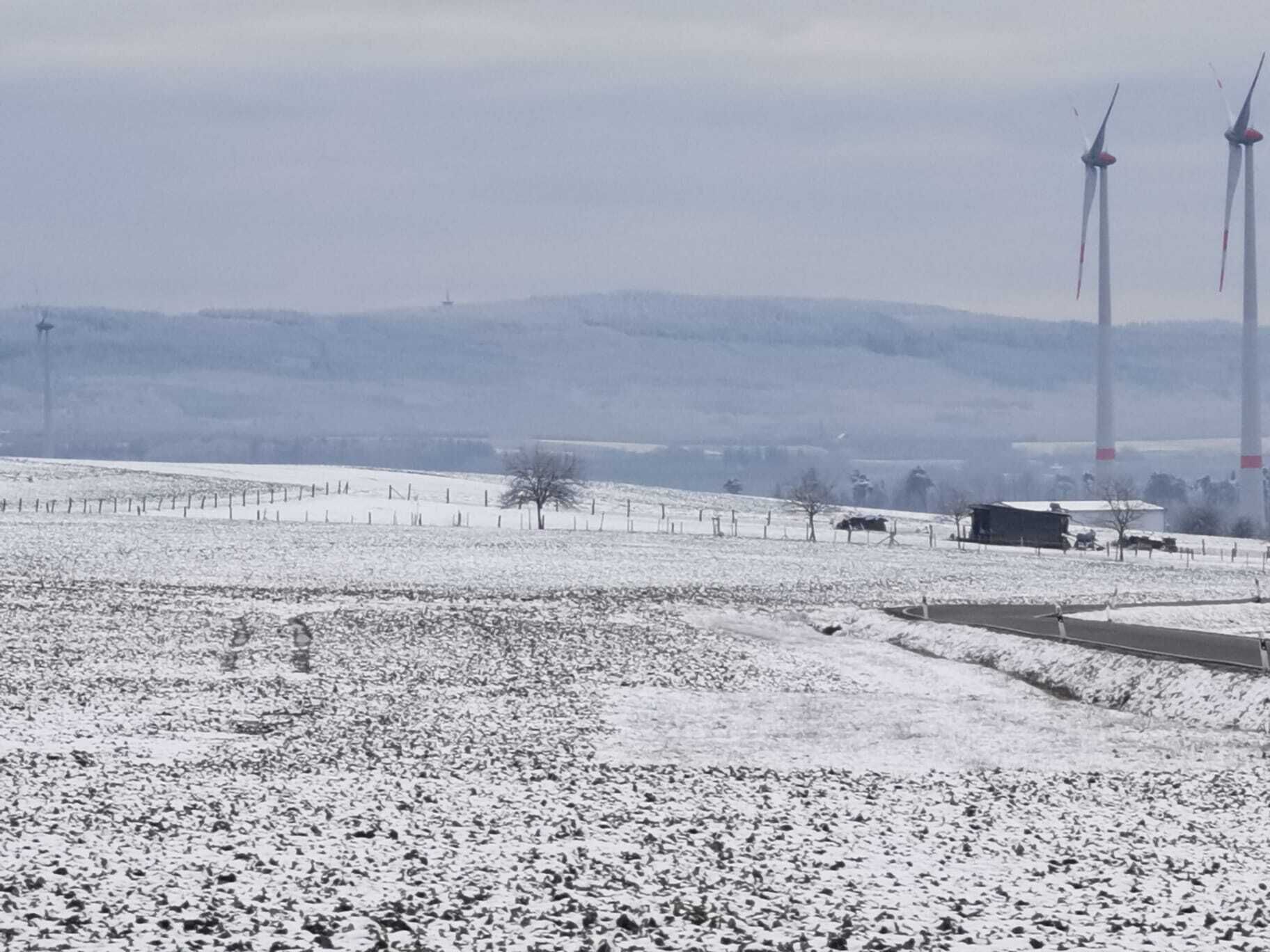 Un paysage enneigé avec des éoliennes, une clôture et un bâtiment.