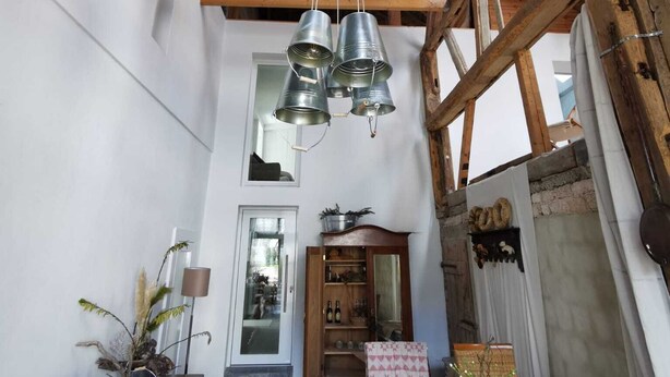 Un interior rústico con vigas de madera a la vista, un comedor con mesa y sillas, y un pasillo que conduce a una puerta.