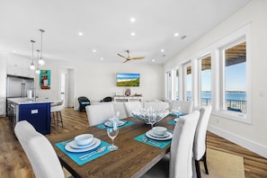 A modern kitchen with white cabinets, a blue island, and a dining area with a wooden table set for six. - 🌞🌴Sound Views | Golf Cart | Community Pool | An Island in the Sun🌞🌴 (Navarre)