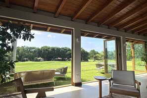 Eine geräumige Terrasse mit Blick auf ein grünes Feld, Holzbalkendecke und moderne Möbel.