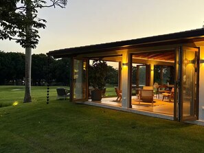 Ein modernes Haus mit Glasfassade, einer Terrasse und Gartenmöbeln sowie einem gepflegten Rasen.
