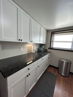 A kitchen with white cabinets, a black countertop, a window with blinds, and a trash can. - Ruby's Garden 2 min walk to Wrigley Field (Chicago)