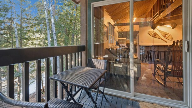 A wooden deck with a glass door leading to an interior with a kitchen and seating area. - Ptarmigan Condo w/ Loft and Fireplace (Whitefish)