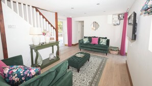 Ein Wohnzimmer mit Treppe, grünem Sofa, Ottoman und einem gemusterten Teppich.