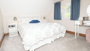 Ein Schlafzimmer mit einem Bett, Nachttischen, einem Schminktisch, einem Spiegel und einem Fenster mit Vorhängen.