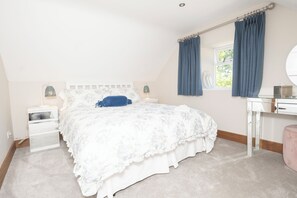 Ein Schlafzimmer mit einem Bett, Nachttischen, einem Schminktisch, einem Spiegel und einem Fenster mit Vorhängen.