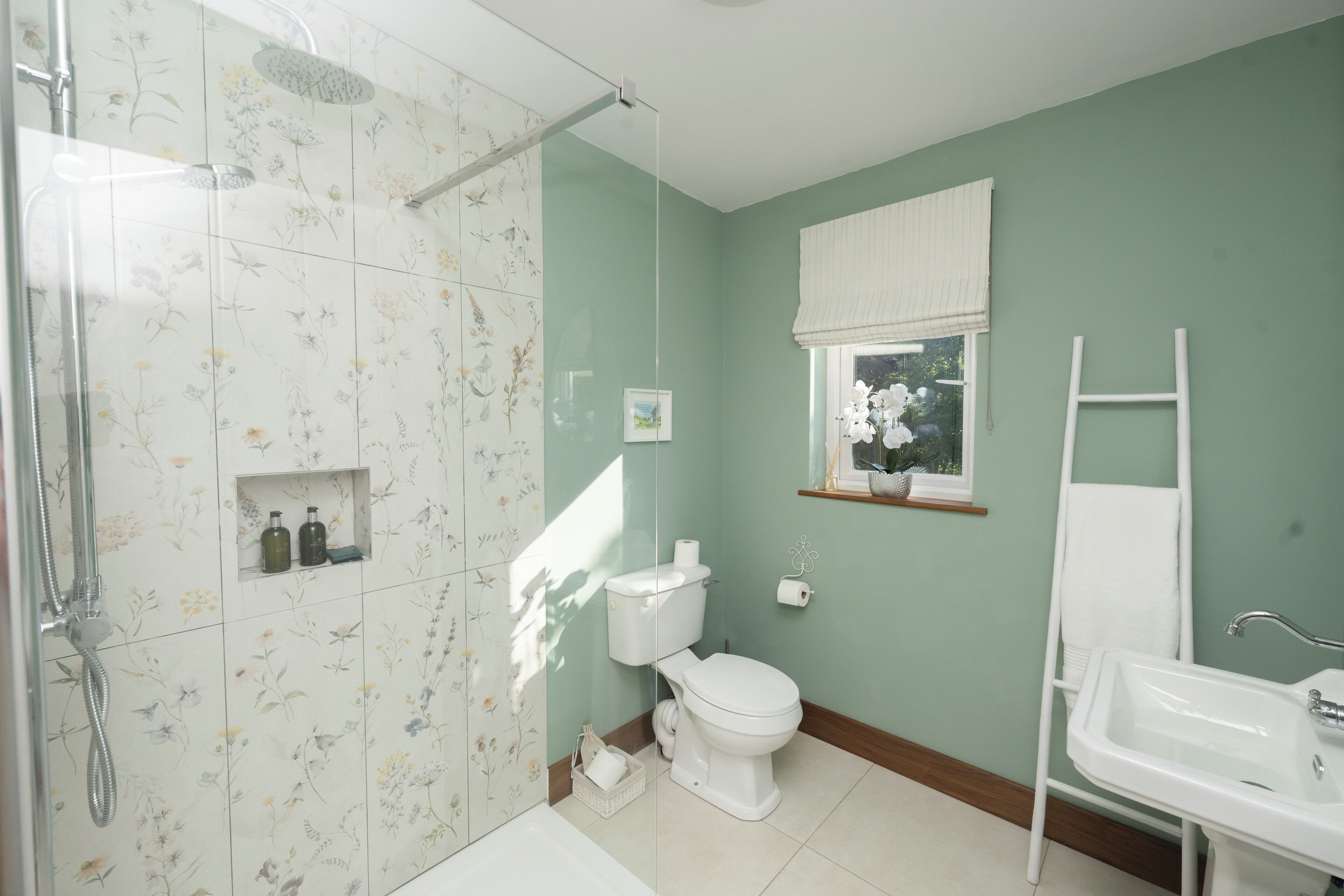 A bathroom with a shower, toilet, sink, and a window with a view of greenery.