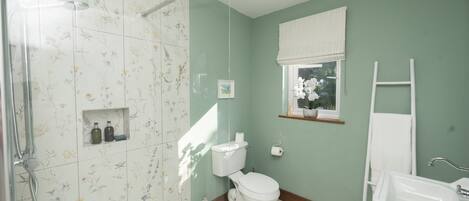 A bathroom with a shower, toilet, sink, and a window with a view of greenery.