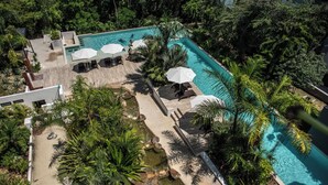 An aerial view of a resort with a swimming pool, lounge chairs, umbrellas, and tropical vegetation. - Luxury Condo in PGA Golf Resort | Bahia Principe (Akumal)