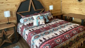 Una habitación estilo cabaña de madera con una cama que tiene un cabecero geométrico, ropa de cama estampada y dos lámparas de noche.