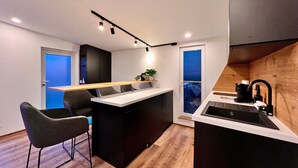 Una cocina moderna con una isla central, taburetes de bar, horno empotrado y ventana con vistas.