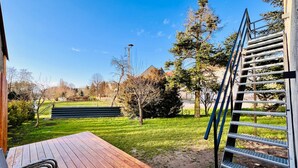 Una terraza de madera con una escalera de metal, césped y árboles.