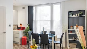 Una cocina moderna con comedor, una mesa de vidrio con fruta y una estantería con adornos.