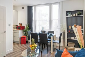 A modern kitchen with a dining area, a glass table with fruit, and a bookshelf with decorative items. - Cosy City Apartment in Central London (London)