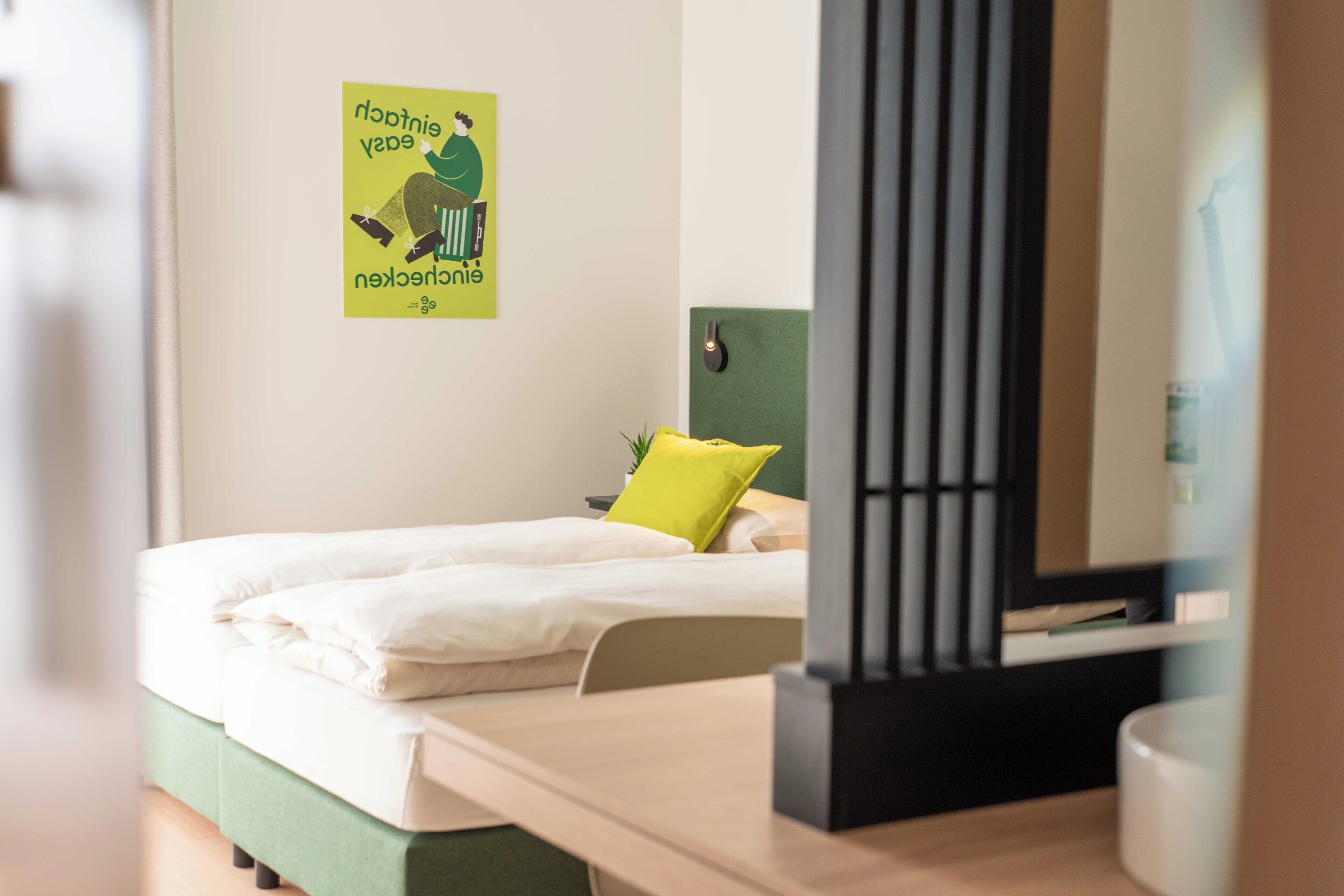A neatly made bed with white linens and a green headboard, a yellow pillow, and a poster on the wall.