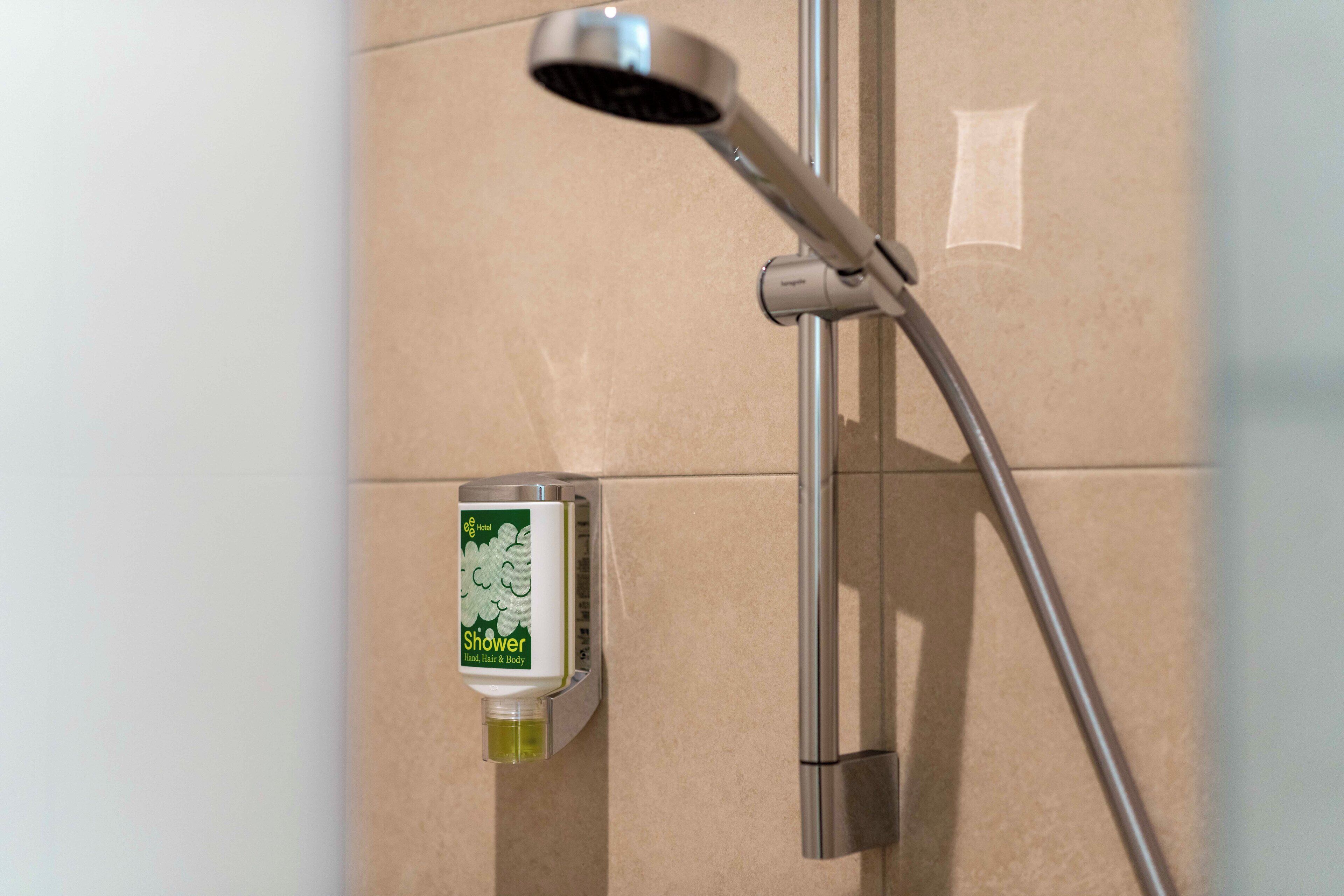 Een douche met een handdouche en een zeepdispenser aan de muur bevestigd.
