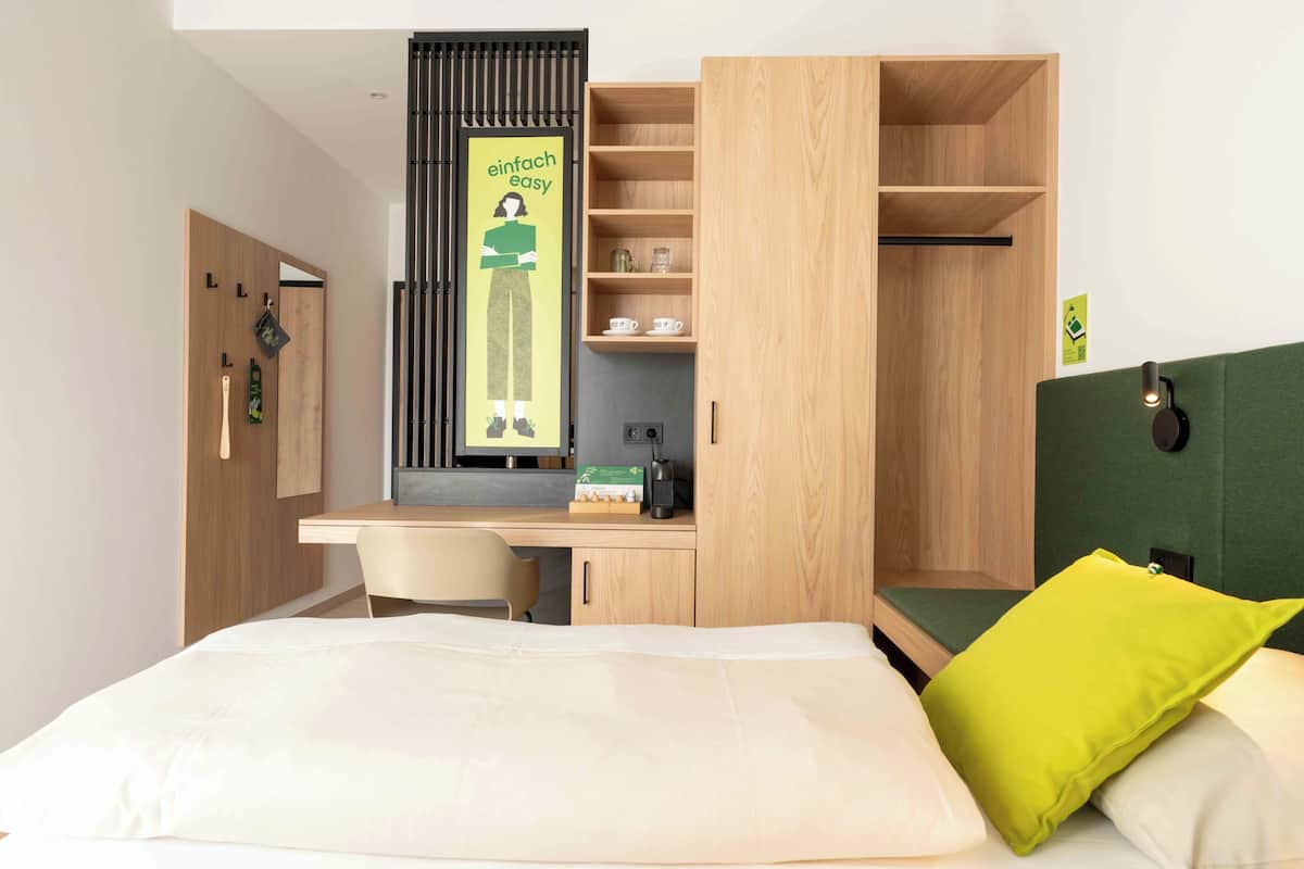 A modern hotel room with a bed, a desk, and a wardrobe.