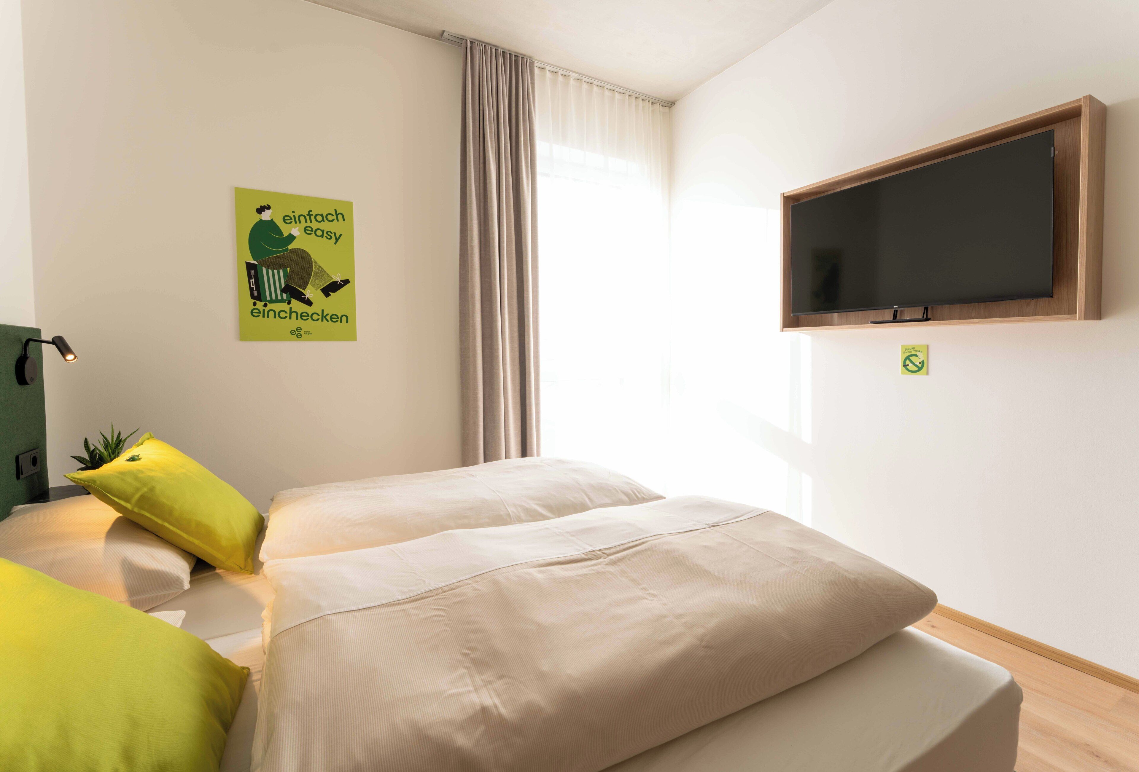 A hotel room with two beds, a TV mounted on the wall, and a window with curtains.