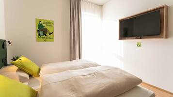 A hotel room with two beds, a TV mounted on the wall, and a window with curtains.