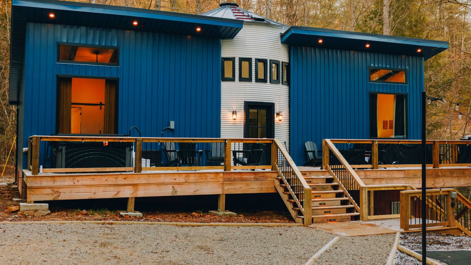 Een moderne houten hut met een blauwe buitenkant, een overdekt terras en een trap naar de ingang.
