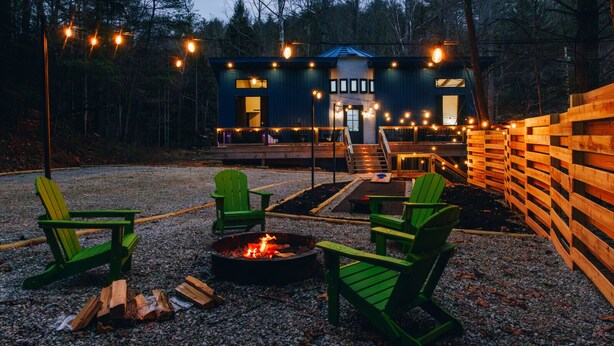 Une cabane avec un foyer et des chaises vertes, située dans un cadre forestier.
