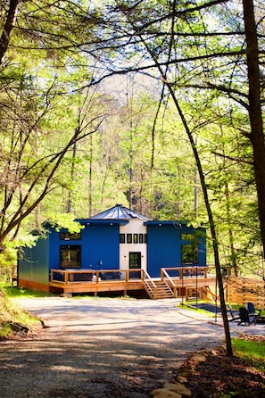 Una baita blu con veranda in legno e tetto in metallo, immersa nel verde.