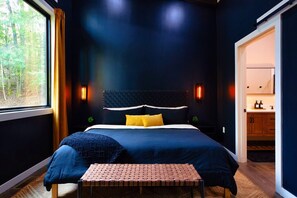 Een slaapkamer met een groot raam, een bed met hoofdeinde, nachtkastjes en een bankje.