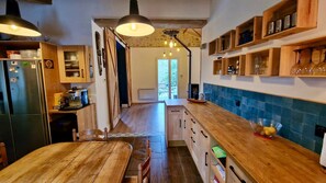 A kitchen with wooden cabinets, a built-in oven, and a dining area with a wooden table and chairs. - Tropical Escape in Dordogne (Le Fleix)