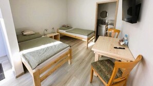 Une petite pièce bien éclairée, avec deux lits simples, une table en bois et une chaise.