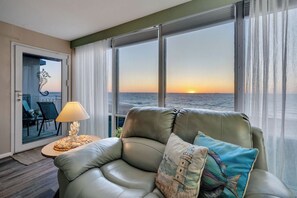 Une pièce avec un canapé en cuir, une lampe et une vue sur le coucher de soleil sur l’eau.