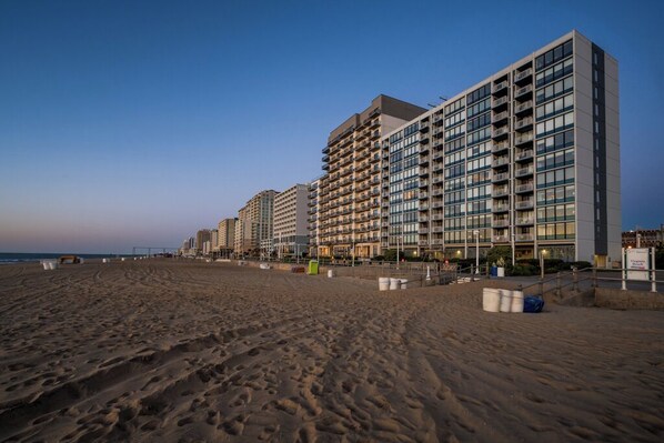 Un hôtel situé en bord de mer, composé de plusieurs immeubles de grande hauteur, avec une plage de sable fin et un ciel dégagé.