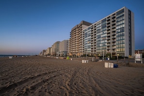 Un hÎtel situé en bord de mer, composé de plusieurs immeubles de grande hauteur, avec une plage de sable fin et un ciel dégagé.
