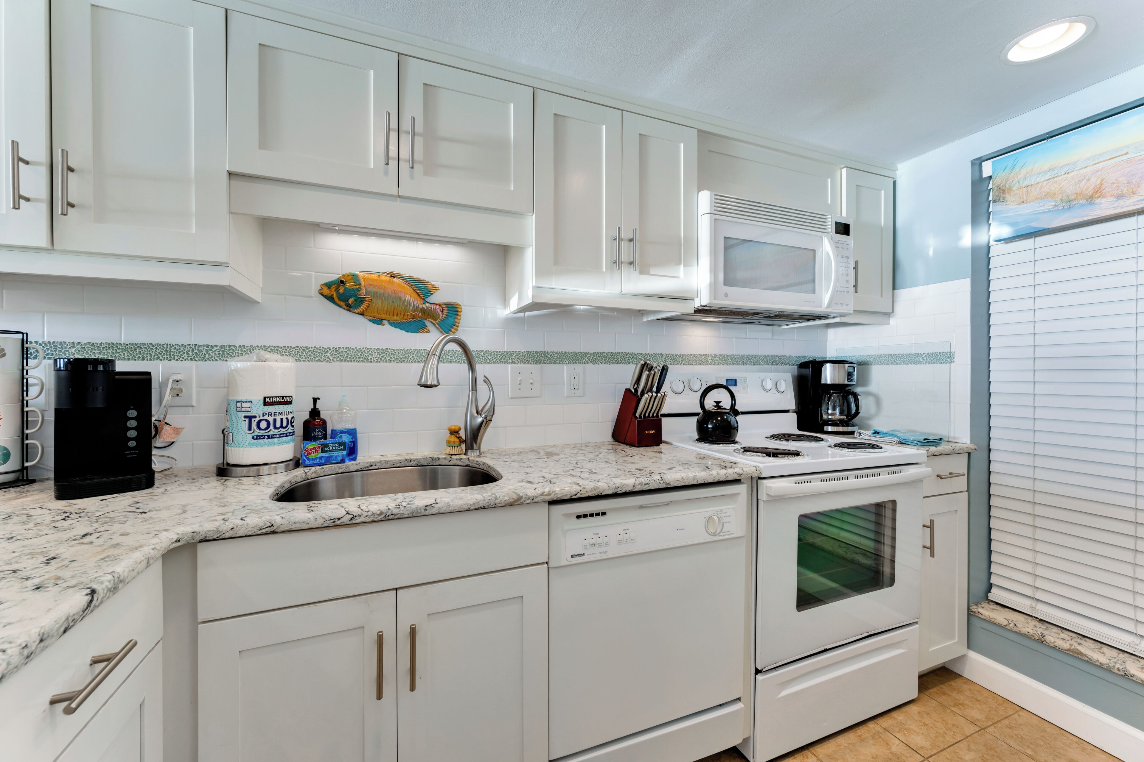 A modern kitchen with white cabinetry, a stainless steel sink, a microwave, a kettle, and a coffee maker.