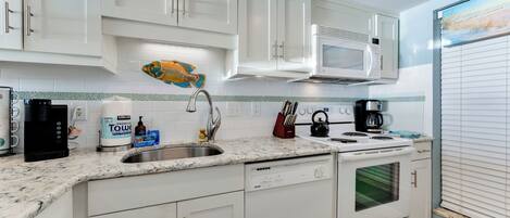 A modern kitchen with white cabinetry, a stainless steel sink, a microwave, a kettle, and a coffee maker.