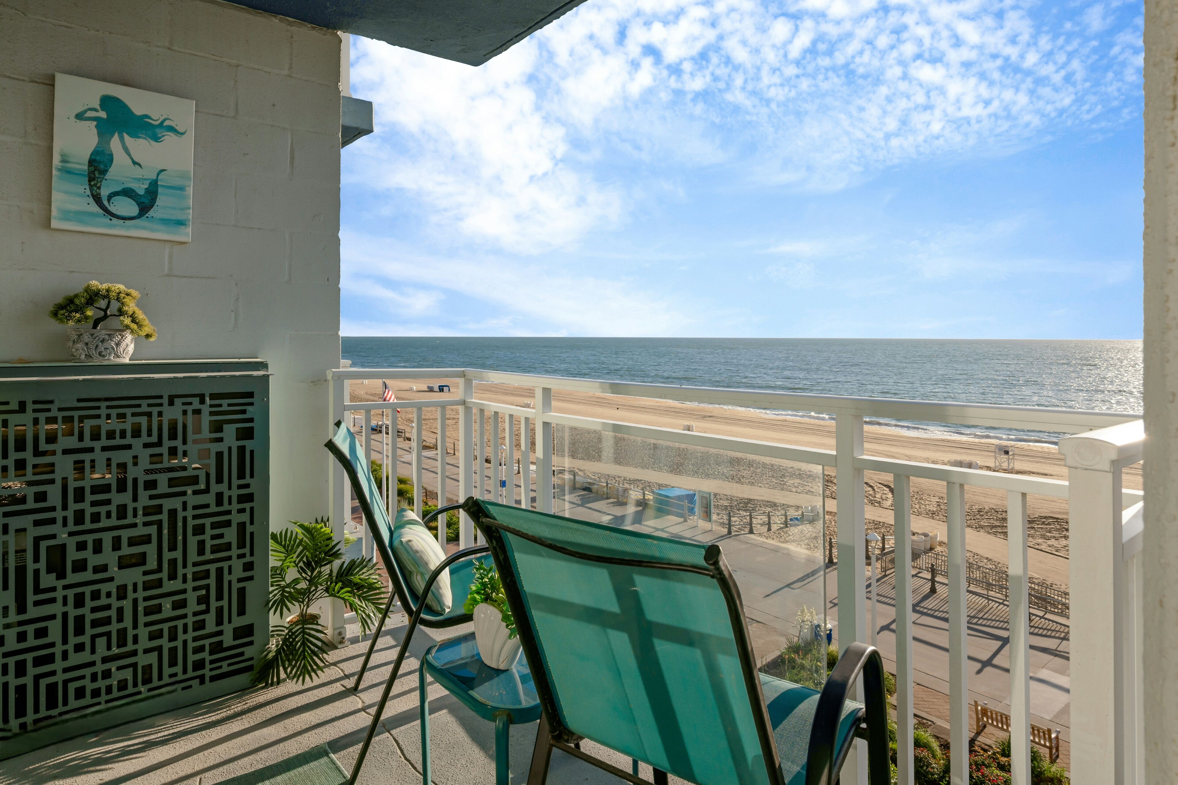 A balcony with a view of the beach and ocean, featuring a chair and a small potted plant.