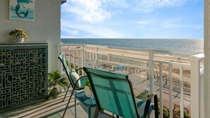 Un balcon avec vue sur la plage et l’océan, agrémenté d’une chaise et d’une petite plante en pot.