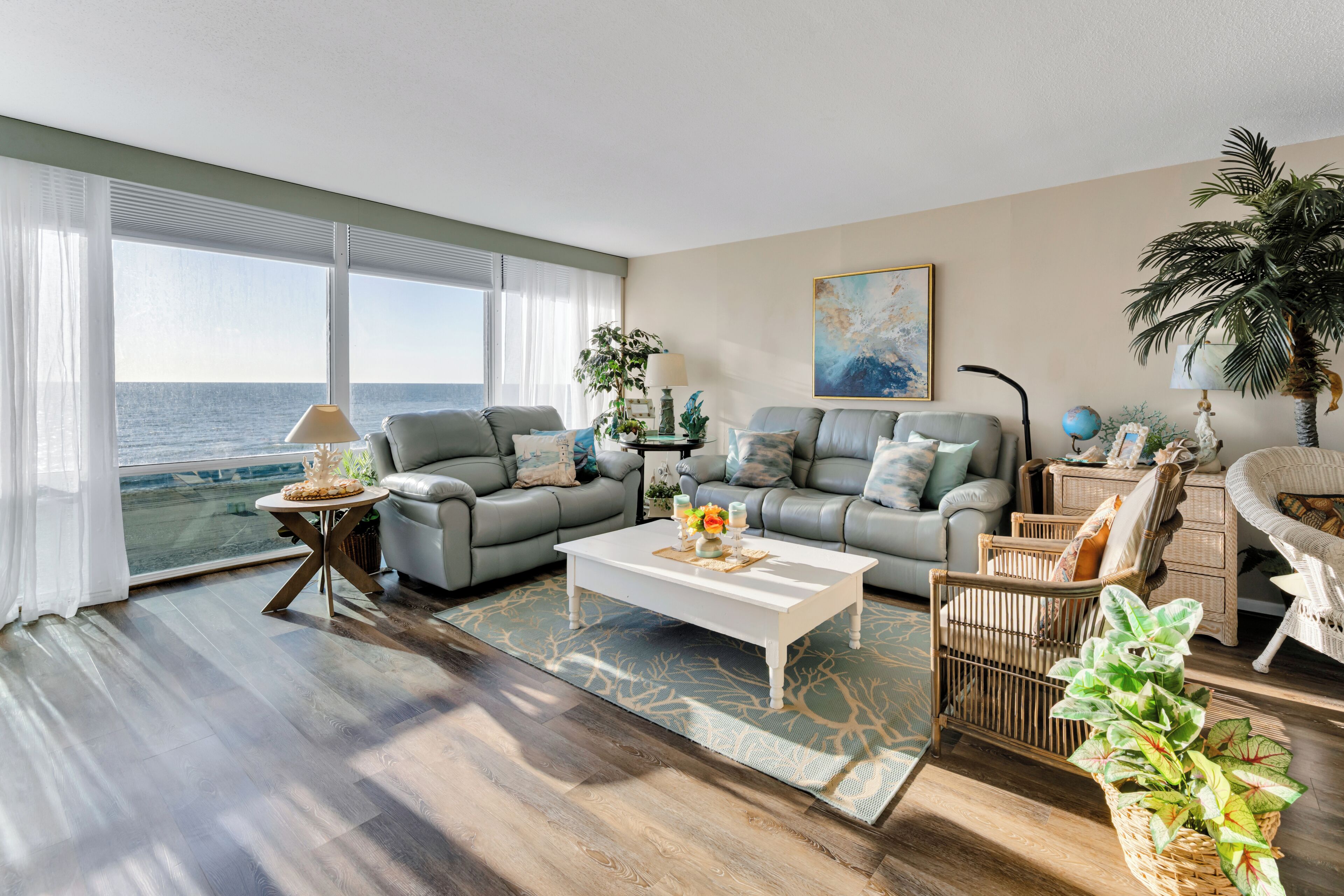 Ein Wohnzimmer mit Meerblick, ein graues Sofa, ein weißer Couchtisch und ein Korbstuhl.