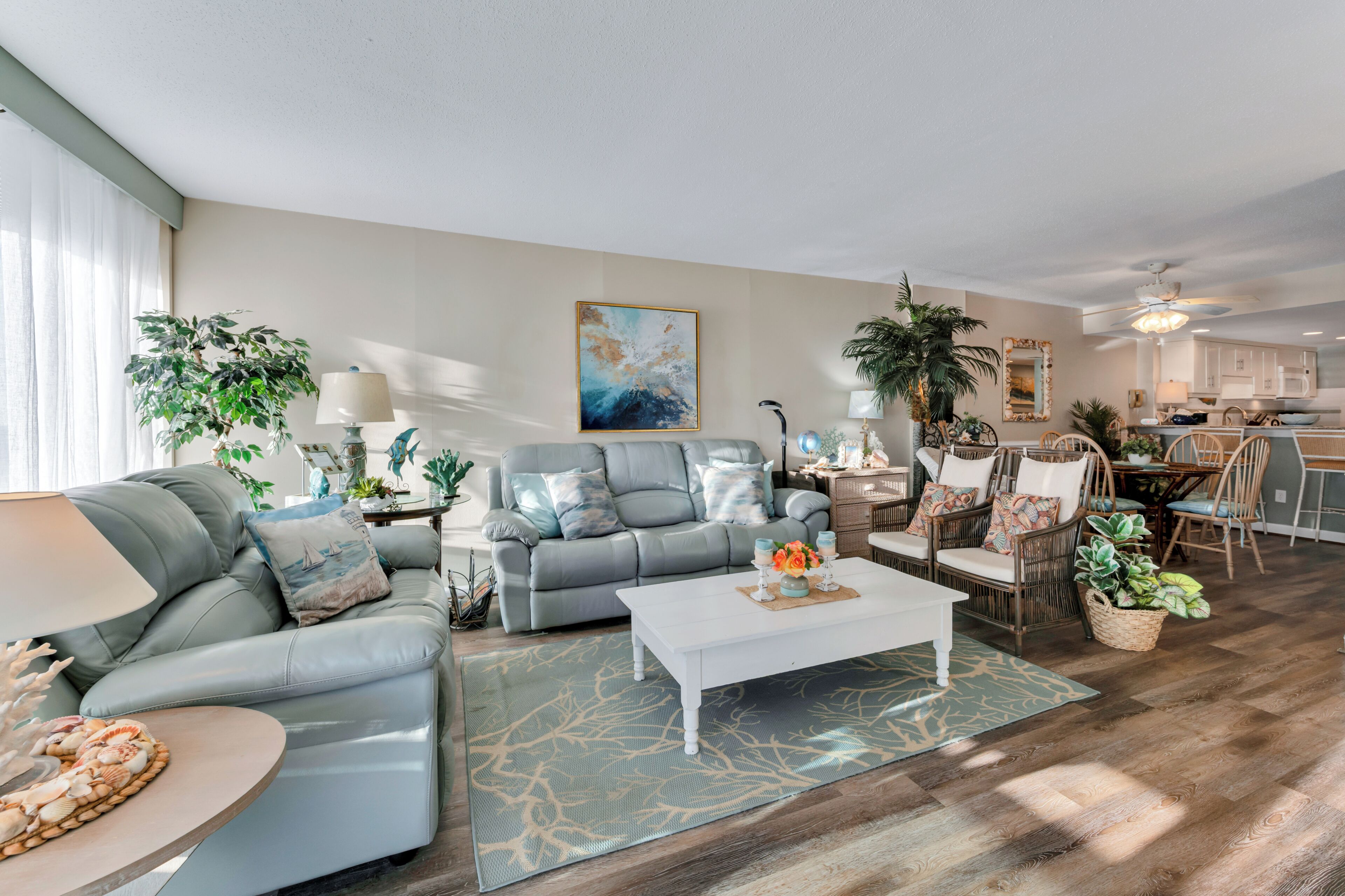 A modern living room with a grey sofa, a coffee table, and a dining area with wicker chairs.
