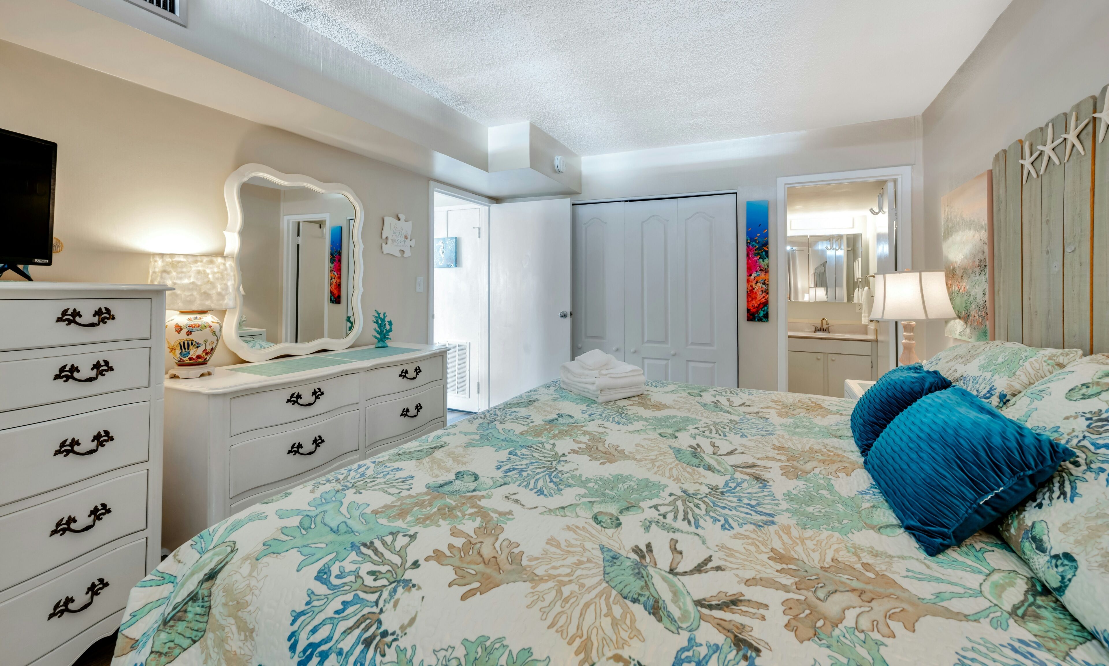 Un dormitorio con cama, cómoda, espejo y una puerta que da a otra habitación.