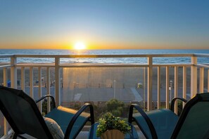 Un balcon avec des chaises et une vue sur l’océan au coucher du soleil.
