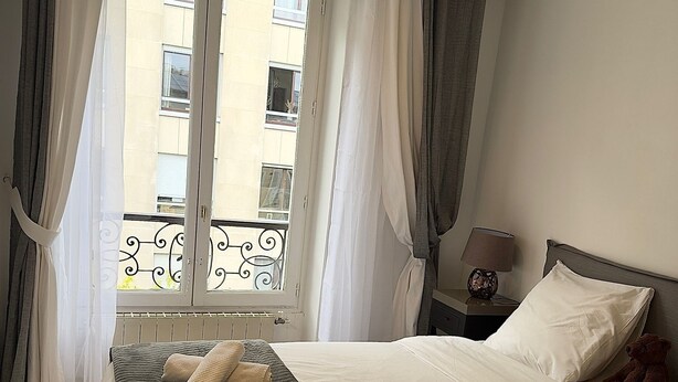 A hotel room with a large bed, a nightstand, a lamp, and a view of the outside. - Paris TROCADERO, 5 mn from the TOUR EIFFEL apartment for 4 people (Paris)